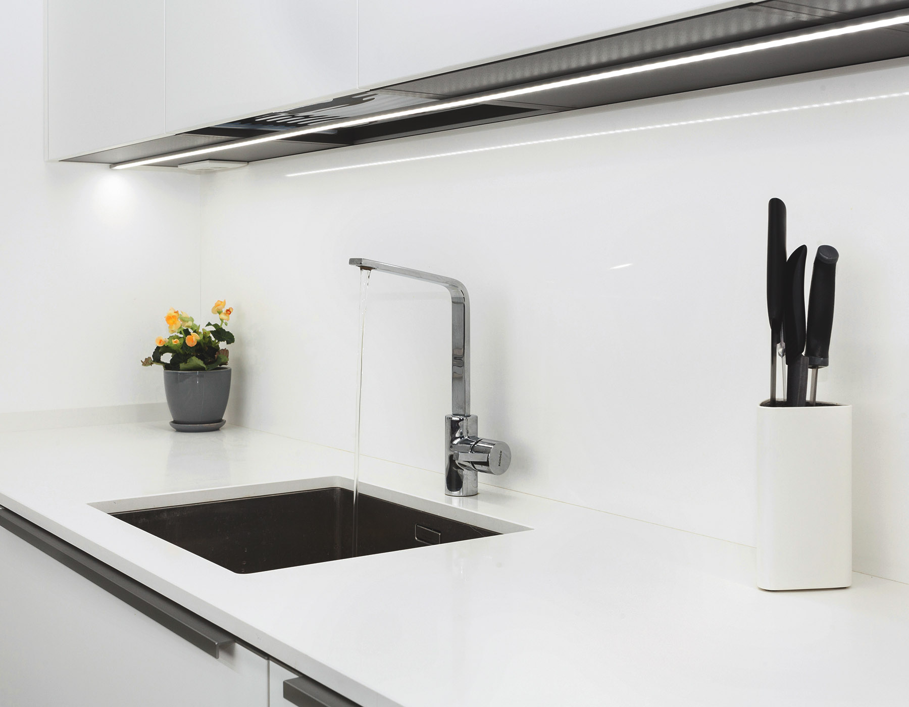 Modern designer chrome water tap over stainless steel kitchen sink. Interior of bright white kitchen